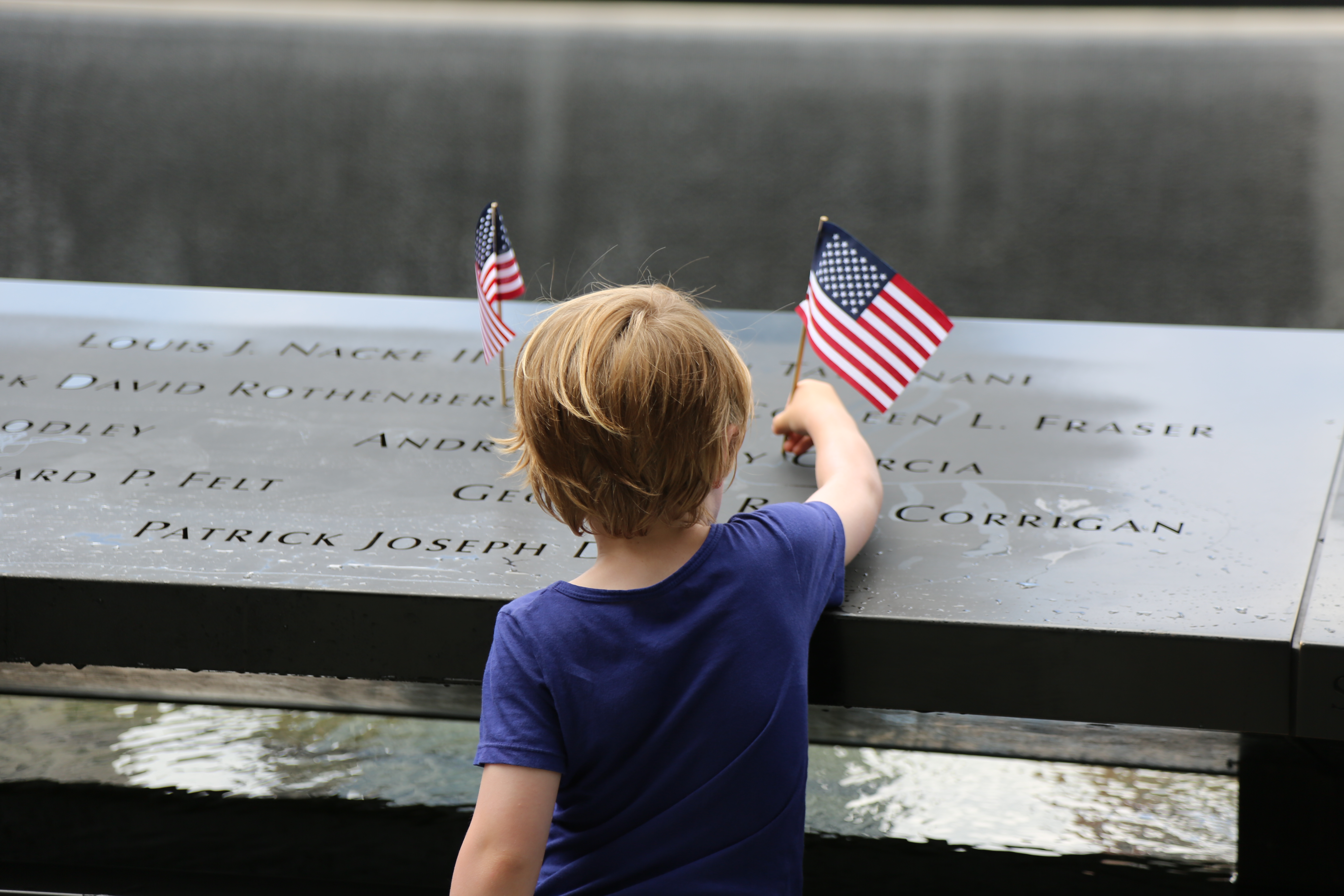 A small child places an American flag at a name on the 9/11 Memorial.