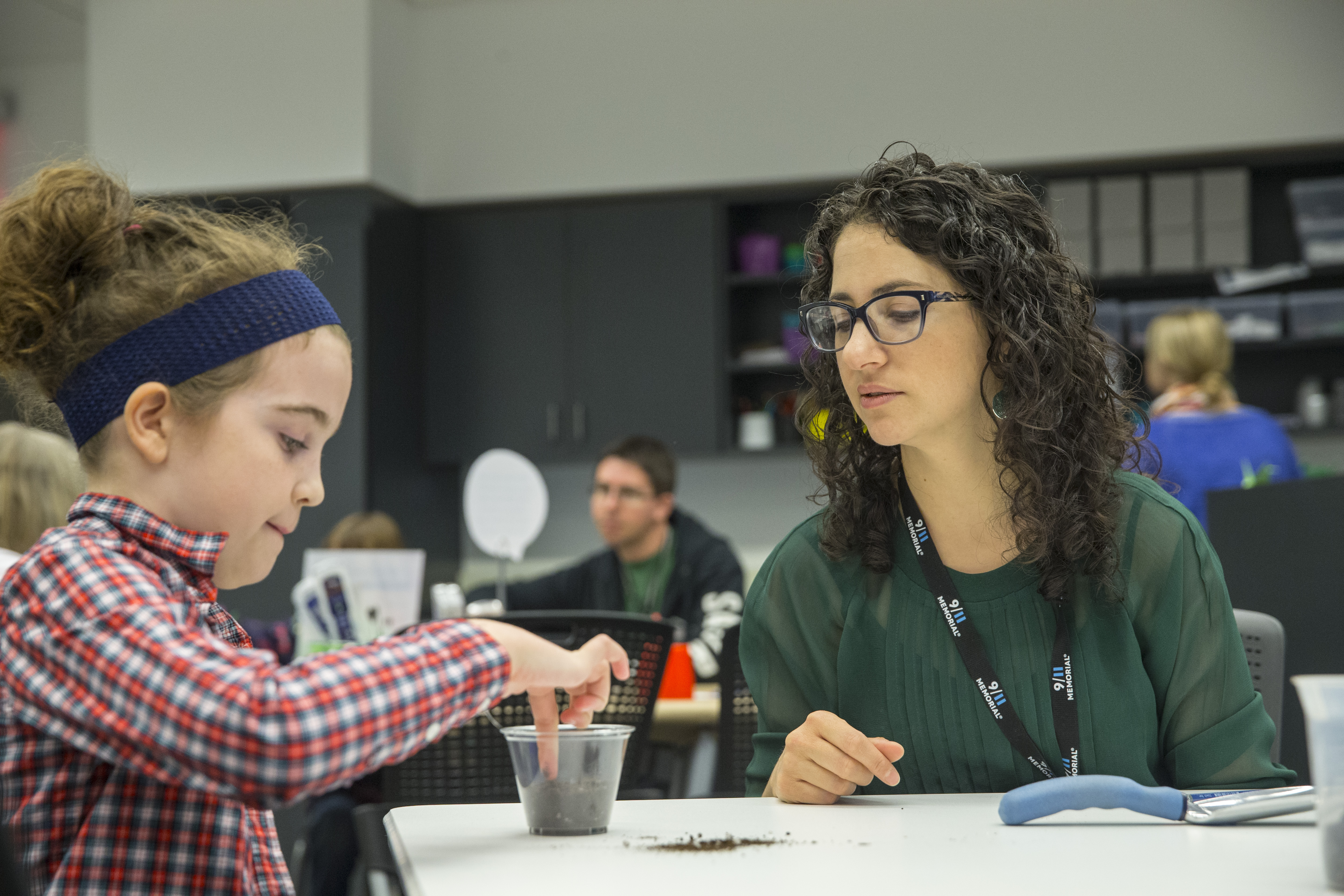 Noaa Stoler, manager of 9/11 Memorial youth and family programs, sits with a girl at the Museum education center. The girl is working with a cup filled with dirt.