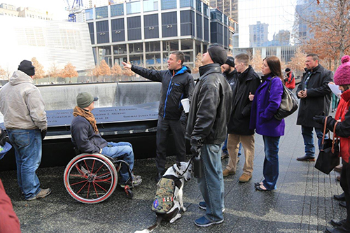 Wounded service members and their families stand beside a reflecting pool on Memorial plaza as they are given a tour.