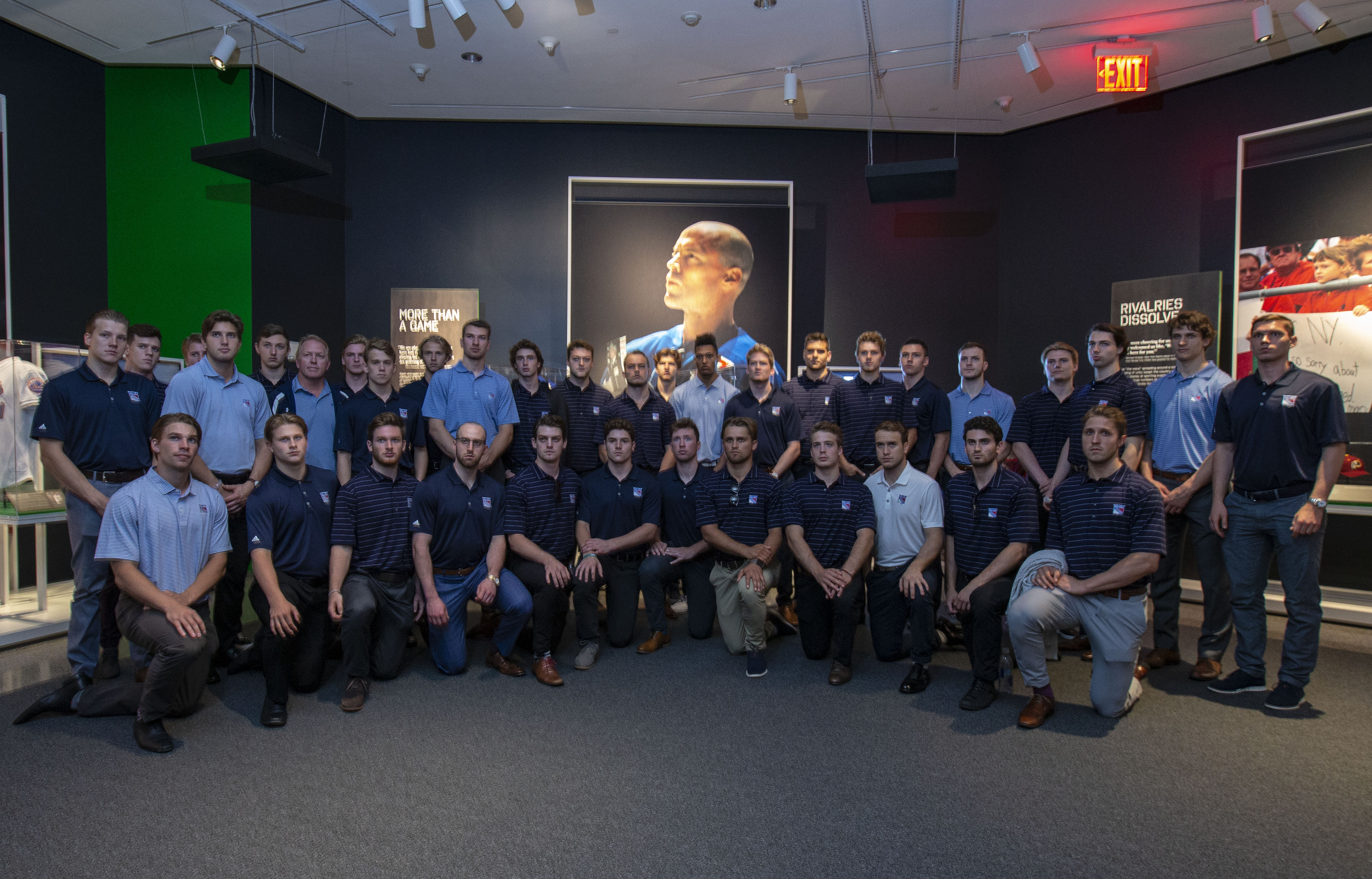 Players and staff from the New York Rangers pose in front of a large photo of Rangers captain Mark Messier at the exhibition, Comeback Season: Sports After 9/11.