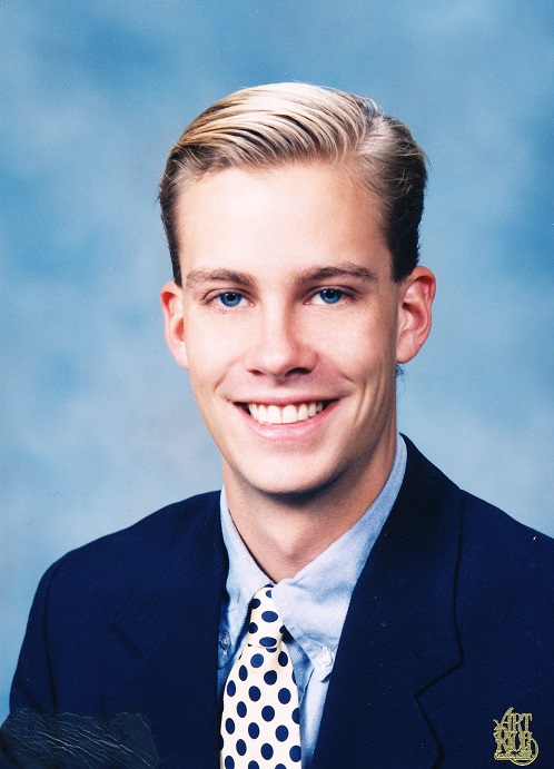 Scott Michael Johnson smiles for a photo in a suit and tie.