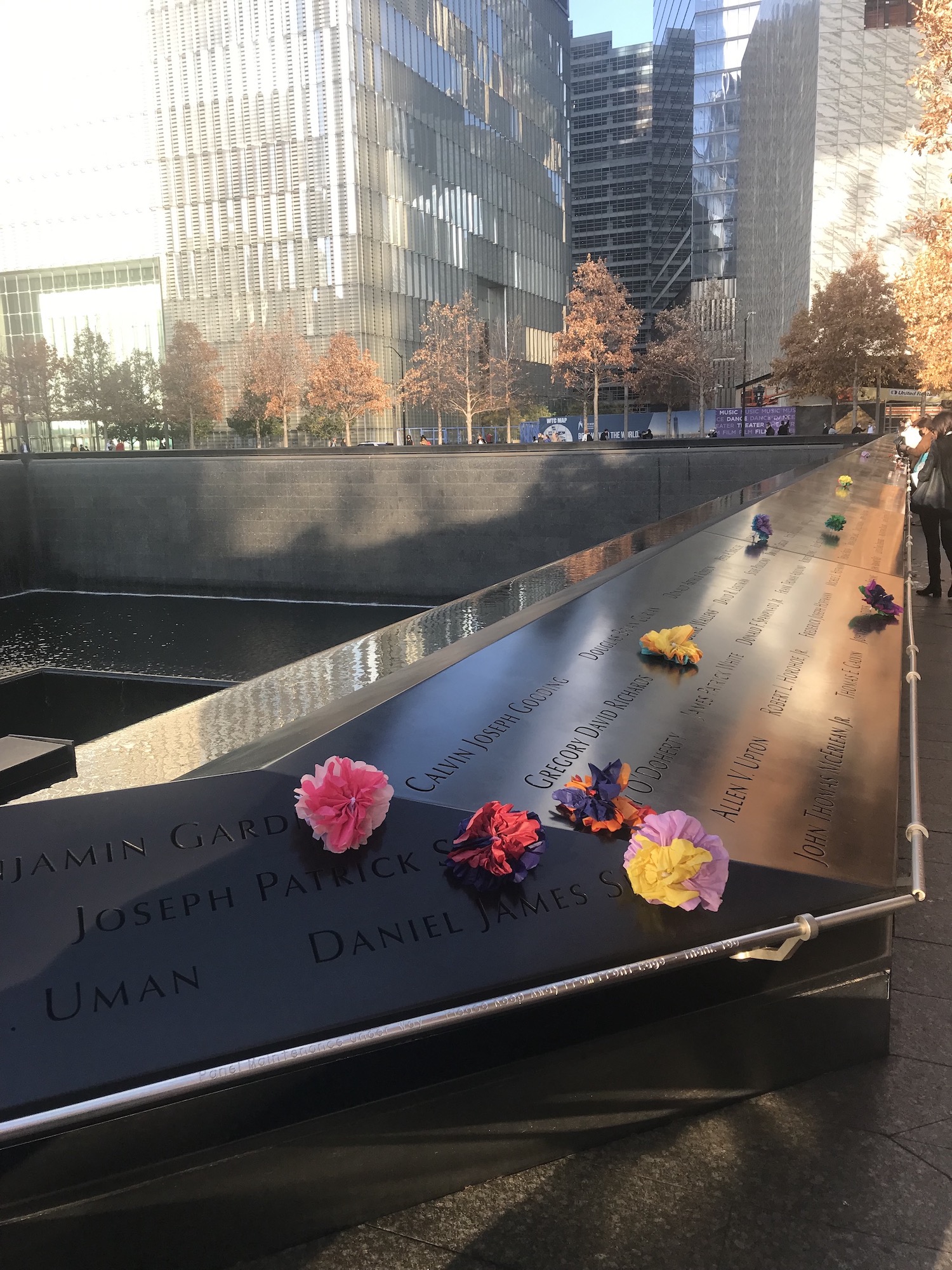 Handmade tissue paper flowers place at names along the Memorial