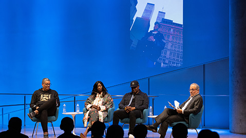 From left: Rocky Bucano, Dr. MC Debbie D, Chuck Creekmur, and Clifford Chanin on stage. Projected on a screen behind them is a photo of a hip hop artist posing in front of the World Trade Center.