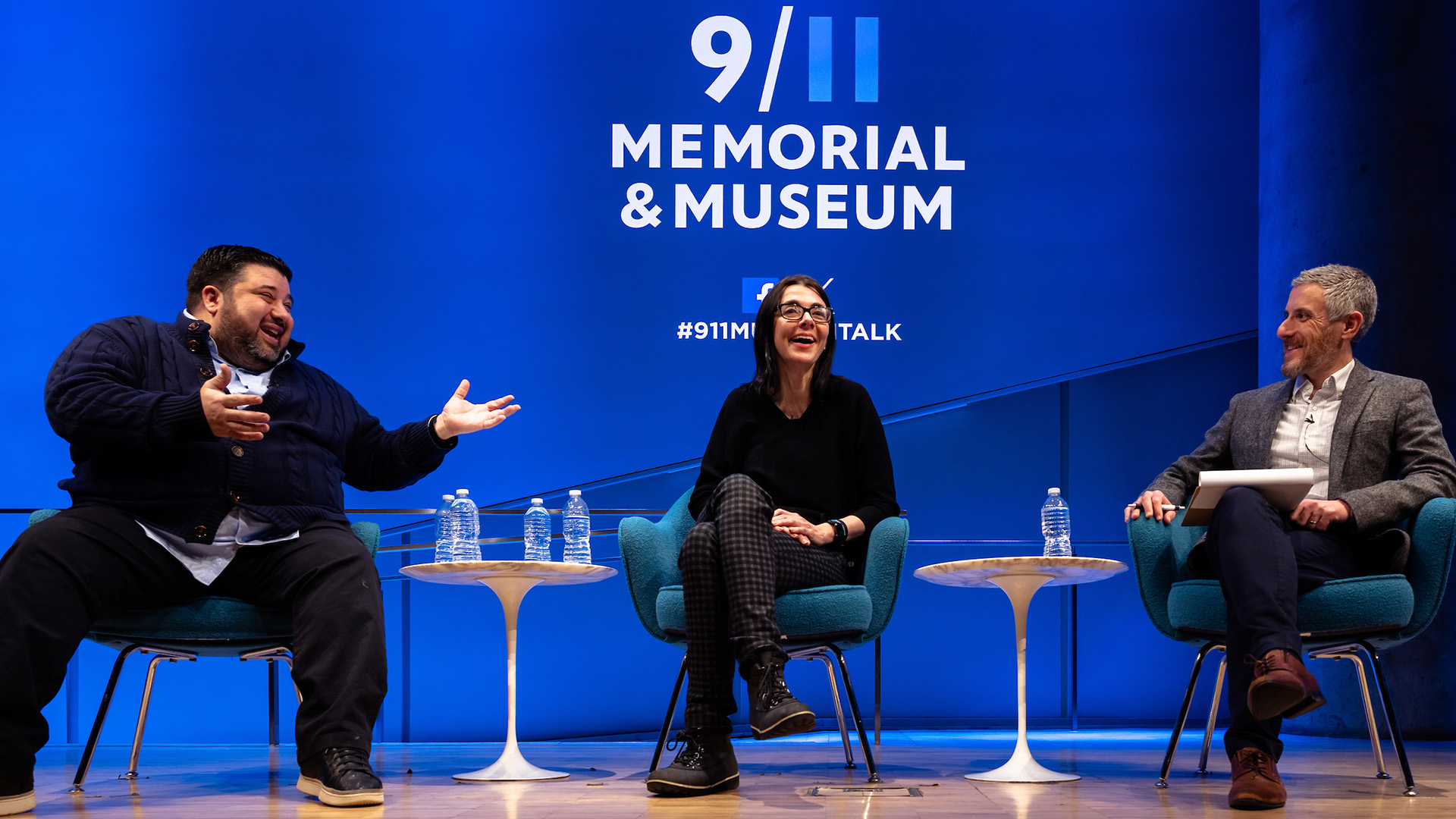 Three speakers, sitting on stage against a blue background displaying the 9/11 Memorial and Museum logo.