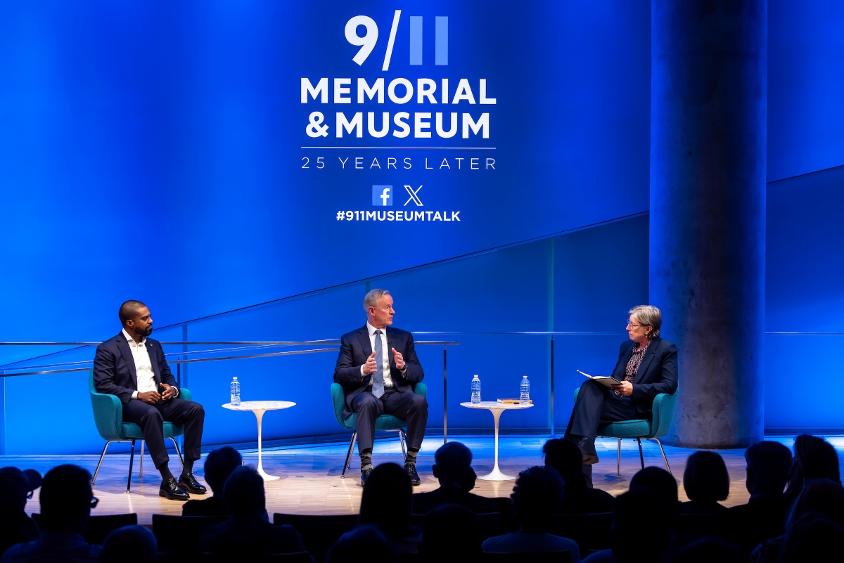Three people on stage under the 911 Memorial & Museum logo on a blue background