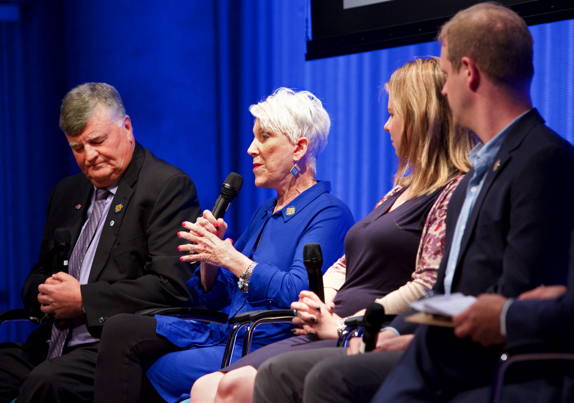 People behind the award-winning new musical “Come From Away” take part in the public program, Come From Away. They include a woman who is holding a microphone and speaking while looking towards the audience. Two men and a woman sit next to her as she speaks.