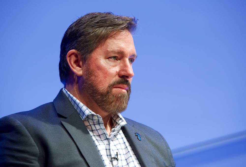 Former special forces commander retired Master Sgt. Scott Neil speaks onstage as he takes part in the public program, The Horse Soldiers. The wall behind him is illuminated light blue.