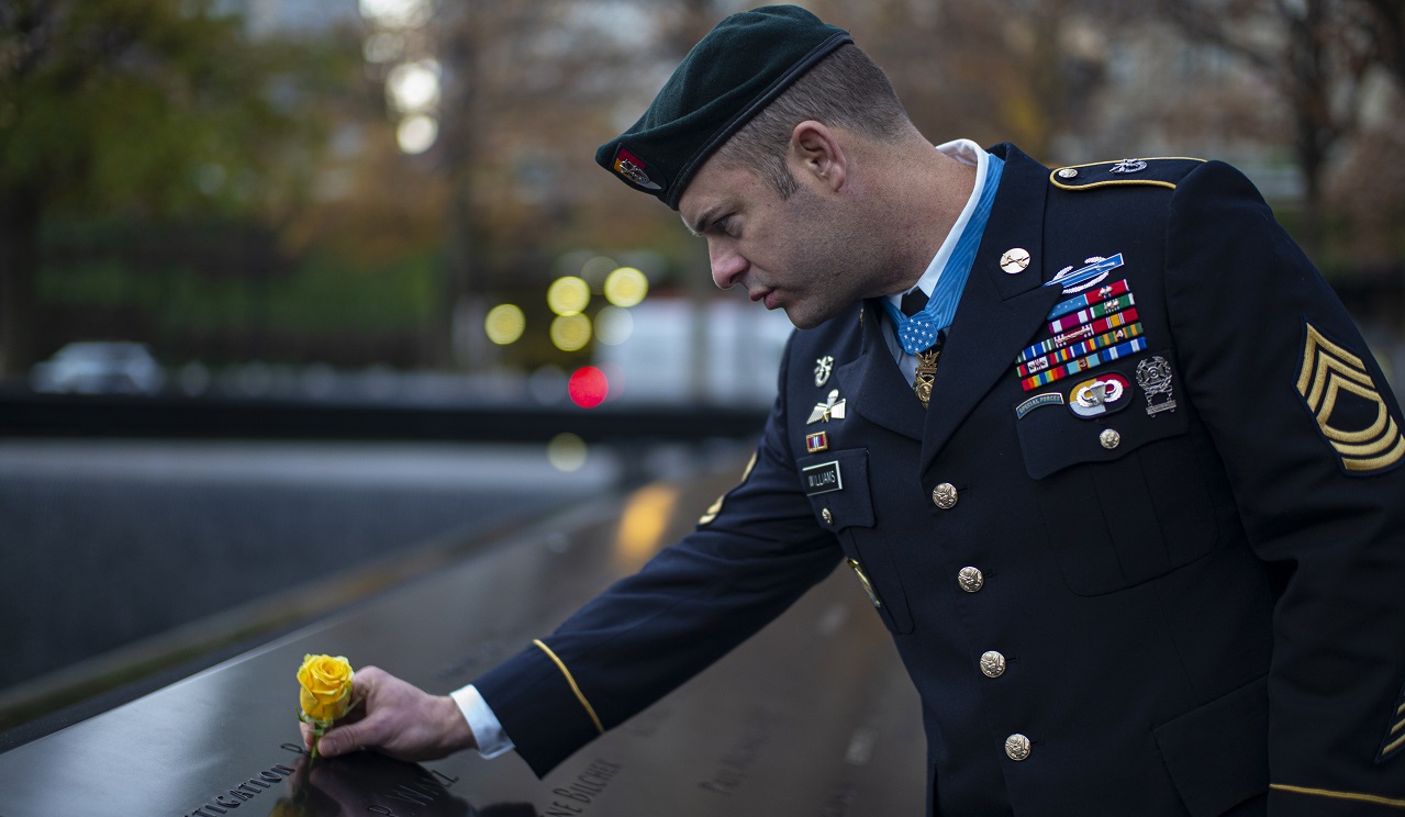 A Medal of Honor recipient in dress uniform places yellow roses on the 9/11 Memorial parapets.