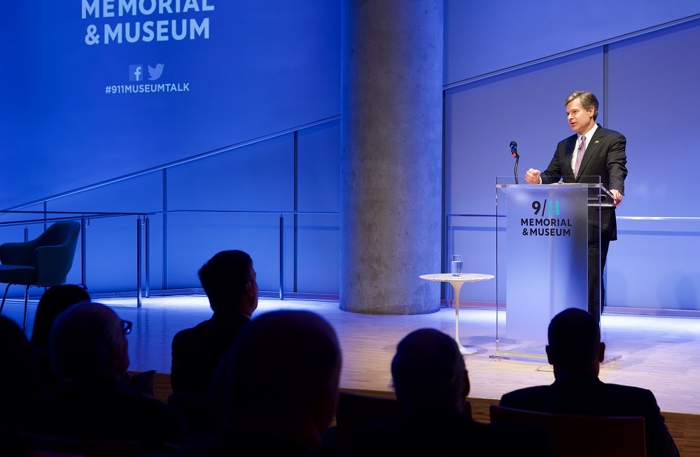 A man stands at a podium while heads of audience members appear in silhouette in the foreground.