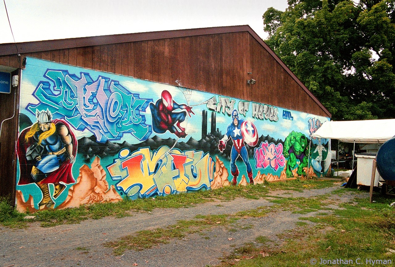 Graffiti-style mural featuring the Twin Towers; the New York skyline; Marvel heroes; and the text "City of Heroes."