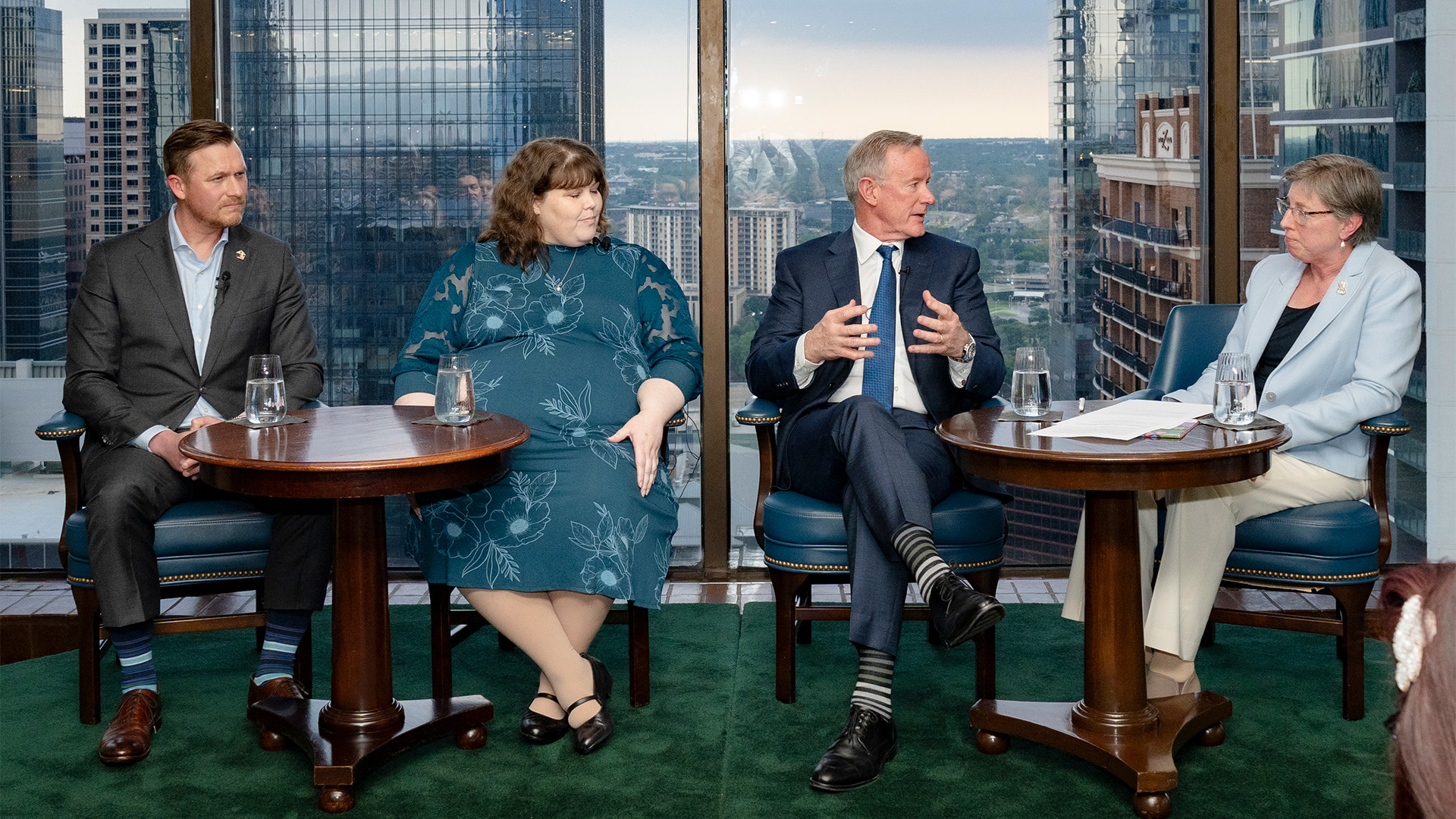 Four speakers, seated in front of a view of the city out of the window behind them