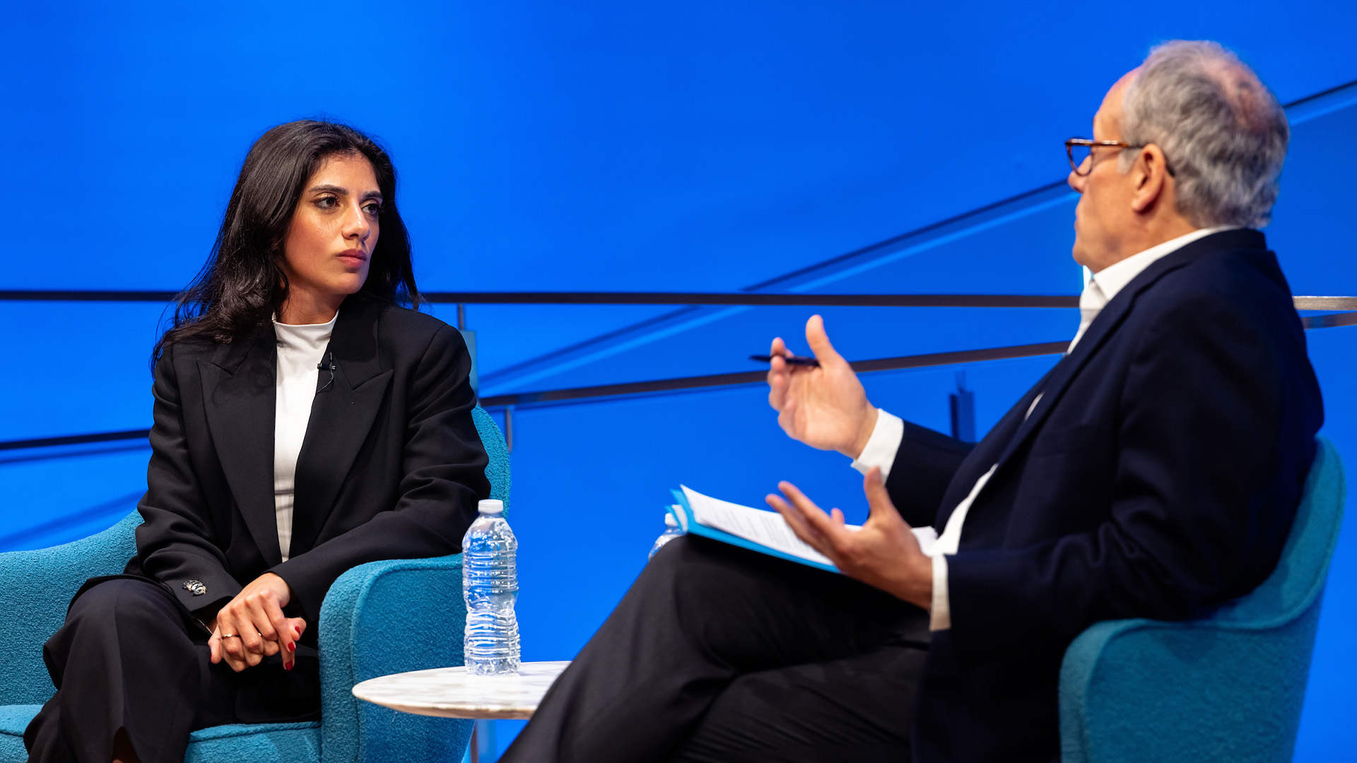 Two speakers sitting in front of a blue backdrop