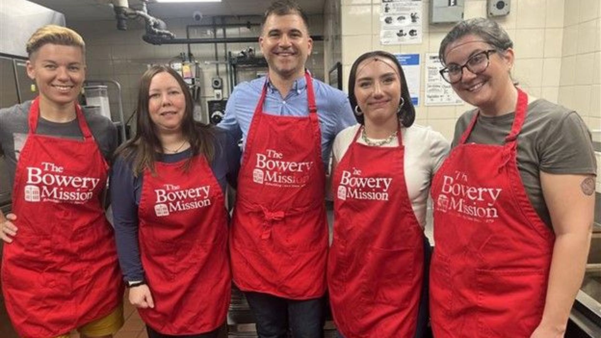Five Visionaries in red Bowery Mission aprons pose together in a kitchen