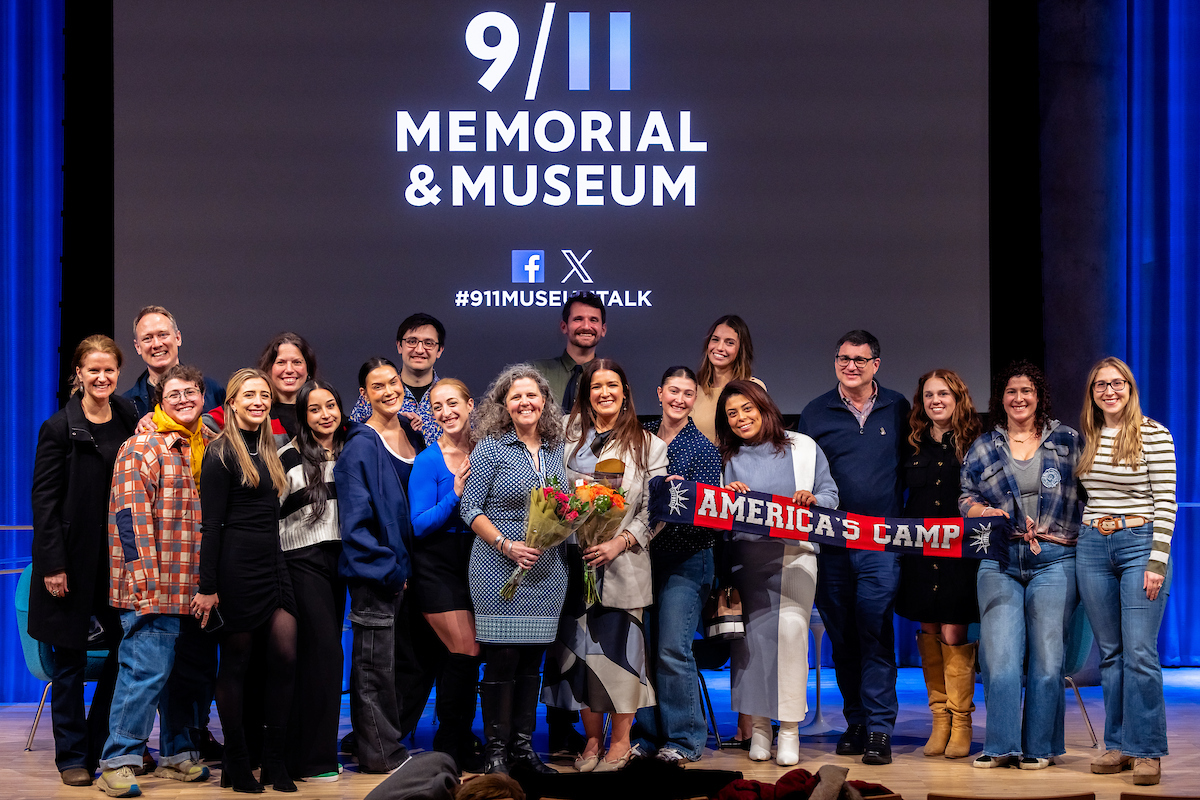 A group shot of around 20 people in front of the 9/11 Memorial & Museum logo screen