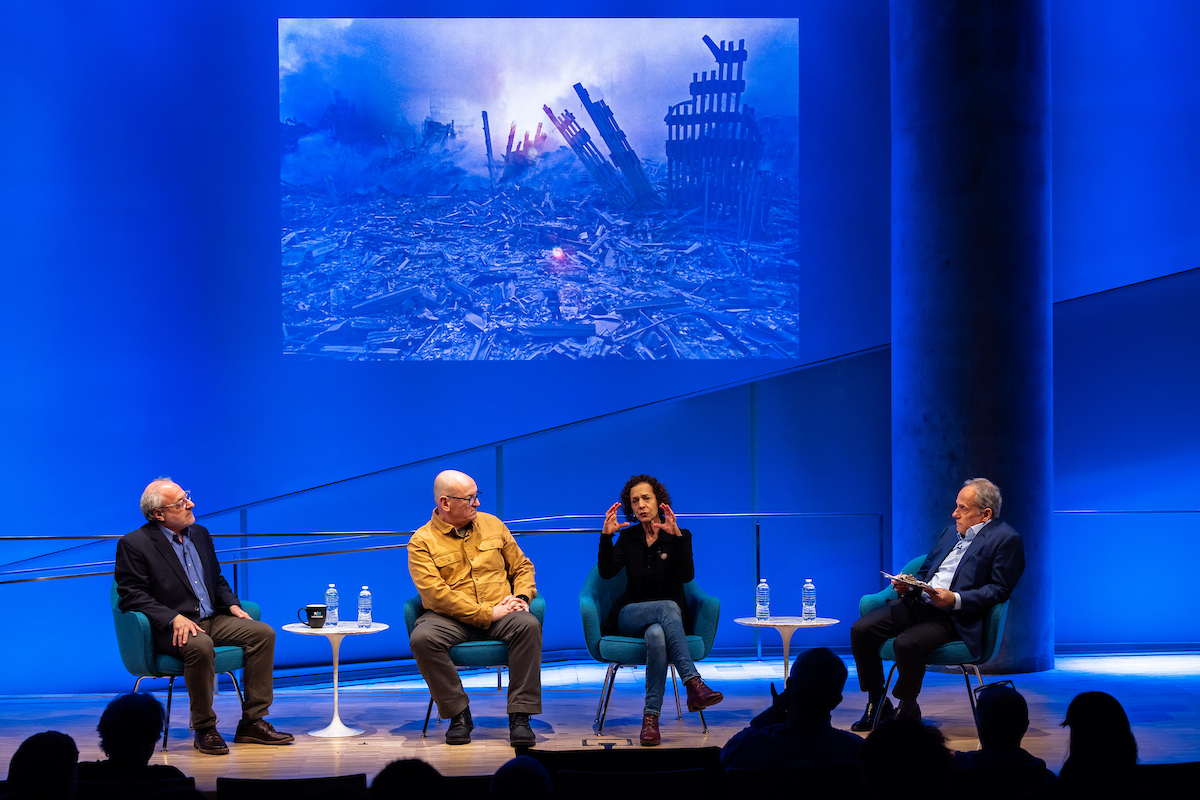 Four people sit on a stage, behind them is a blue banner or screen with 9/11 Memorial & Museum's logo and social icons visible