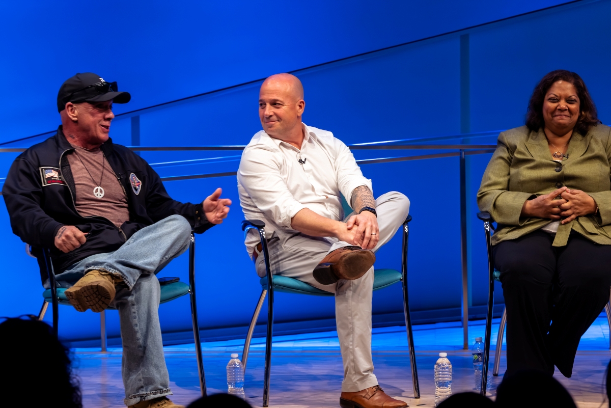 Three people, two men and a woman, talk on stage