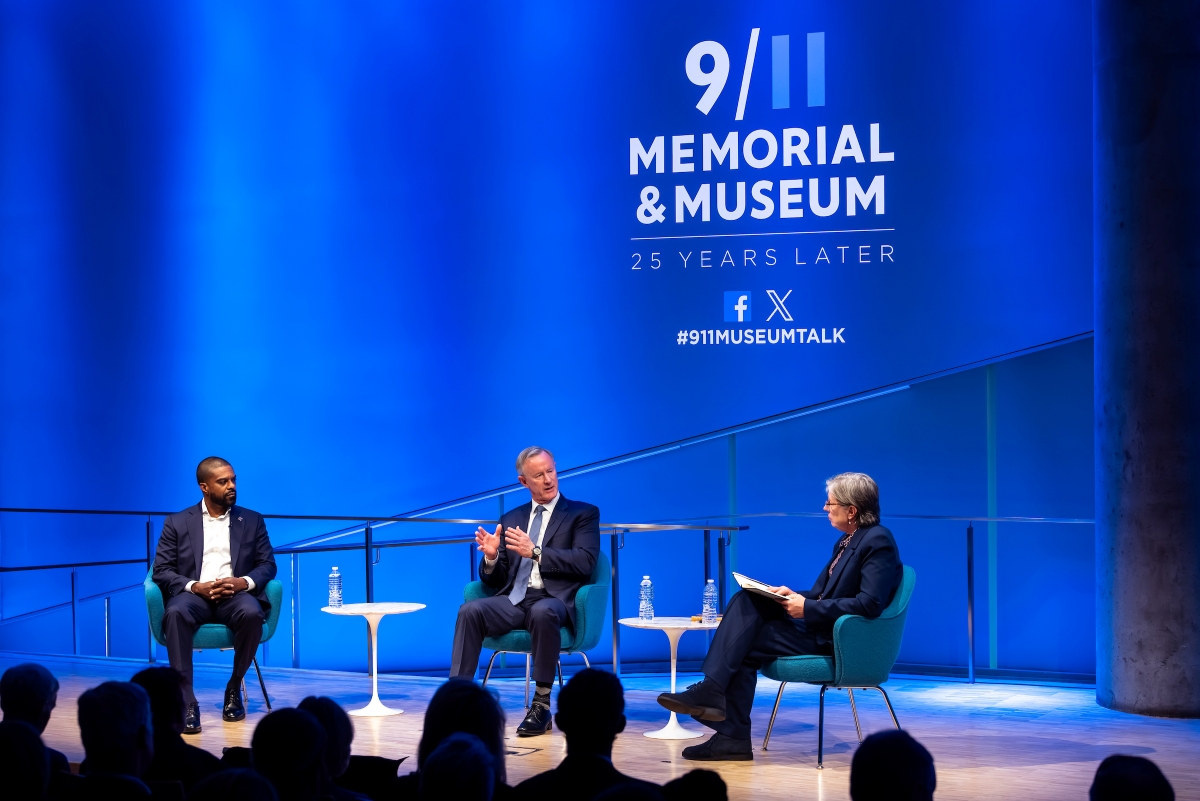 Three speakers sit on stage, engaged in conversation. The 9/11 Memorial & Museum logo is visible above on a blue background.