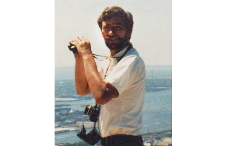 Stephen Knapp holds a pair of binoculars on the rooftop of the North Tower in this old photo. The South Tower can be seen off to the left. Aerial views of New York Harbor and the Atlantic Ocean are seen to the right. 