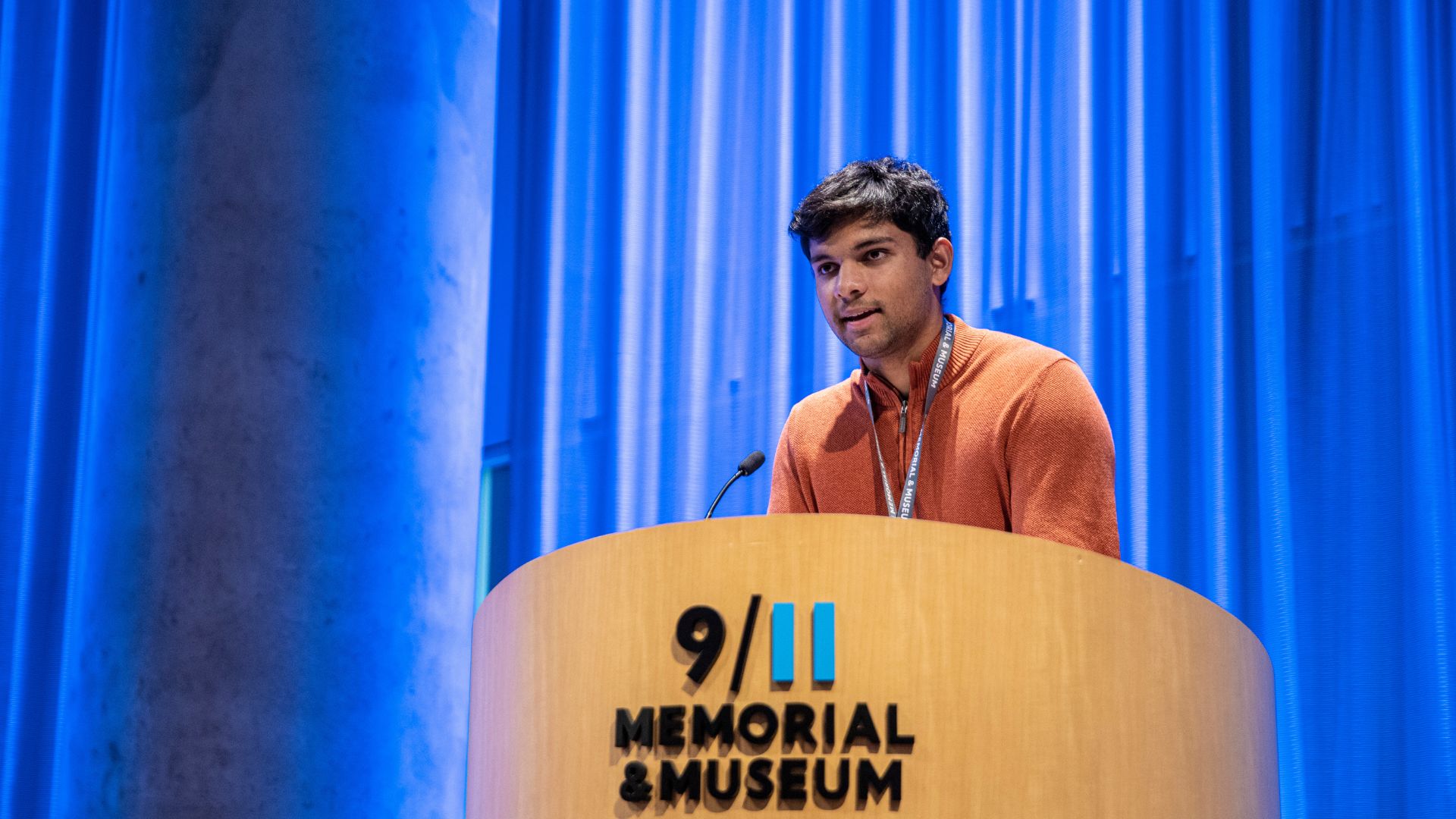 Intern Jack Moses, in orange shirt, stands at Museum auditorium podium 