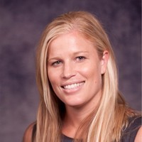 A smiling young woman with long blonde hair in a dark sleeveless dress against a dark background