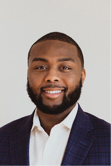 A bearded, smiling young man in a white shirt and navy blue blazer