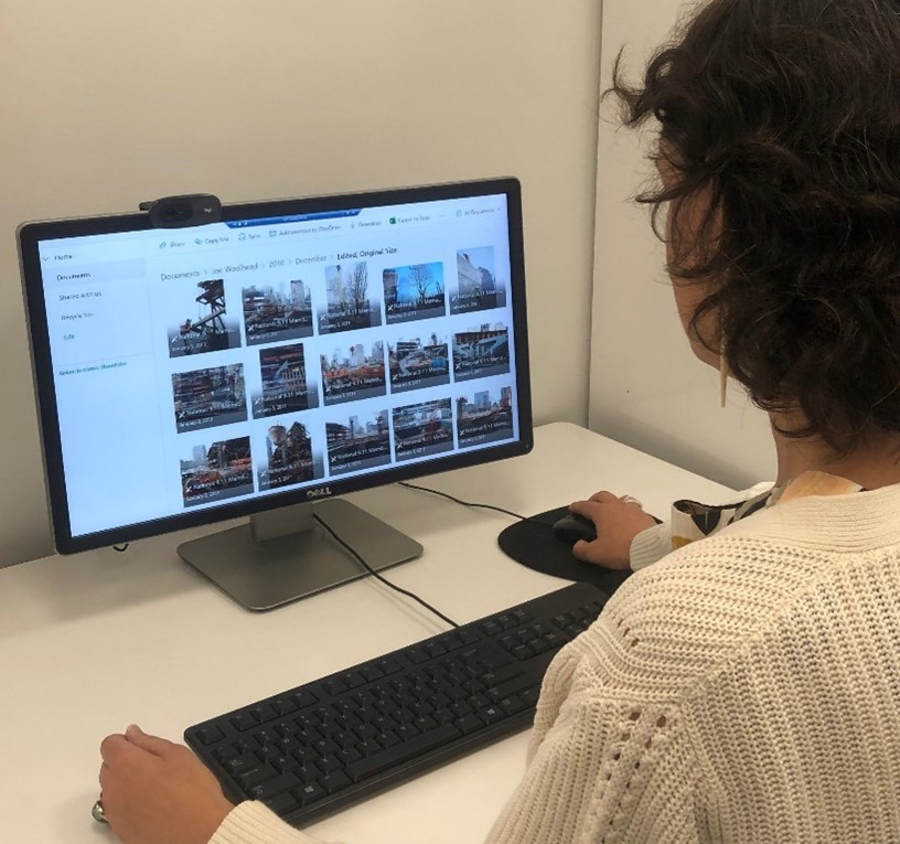 Back and side view of an archivist, wearing a beige sweater, viewing digital assets on a computer screen