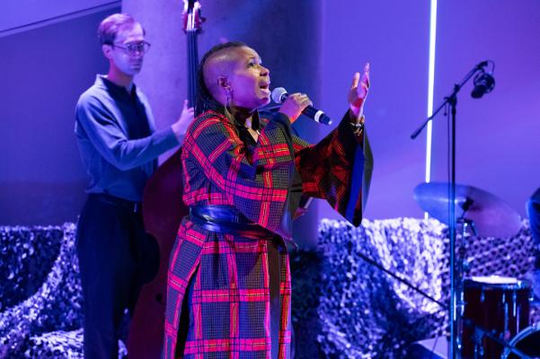 A woman in a blue and red dress raises her arms and sings