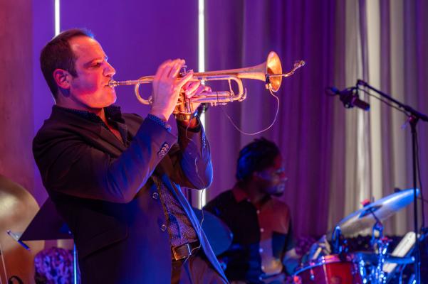 A man leans back slightly, wearing a dark suit playing the trumpet
