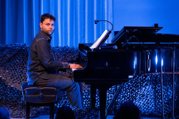 piano player, a man wearing black, plays and faces the audience