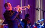 A man leans back slightly, wearing a dark suit playing the trumpet