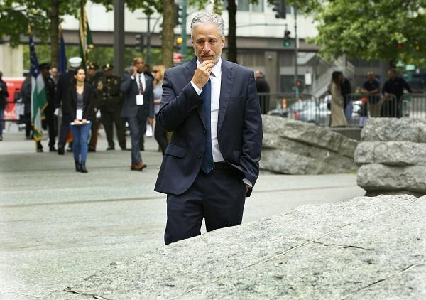 Jon Stewart touches his face as he looks at a granite monolith at the 9/11 Memorial Glade.