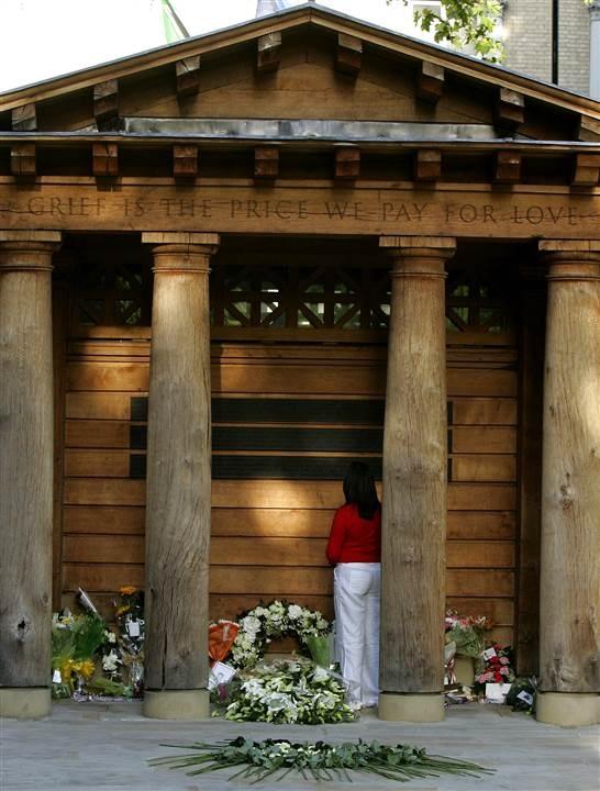 A woman surrounded by wreaths and flowers stands solemnly at the Grosvenor Square Garden memorial in London. An inscription on the memorial reads, “Grief is the price we pay for love.”