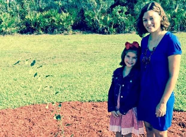 Third-grader Ellie Brinling and guidance counselor Crystal Baugh stand beside a survivor tree planted at Cracker Trail Elementary.