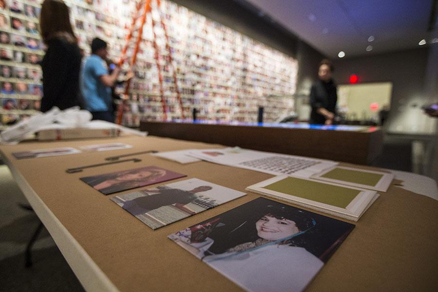 Museum staff install new portraits of 9/11 victims at the Museum’s Memorial exhibition. Several of the portraits can be seen up close on a table as staff members stand beside a ladder in the background.