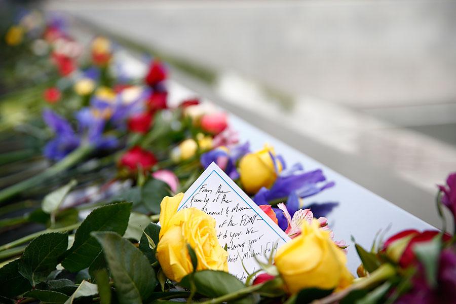 A message sits amid dozens of red, yellow, and purple flowers left on a bronze parapet in tribute to FDNY firefighter Michael Fahy.