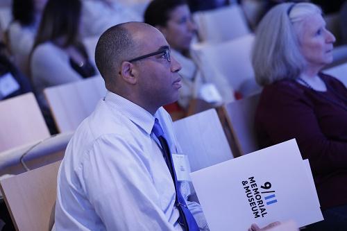 An educator looks towards the stage in the Museum auditorium. He is holding a 9/11 Memorial & Museum folder and wearing a tie and dress shirt.