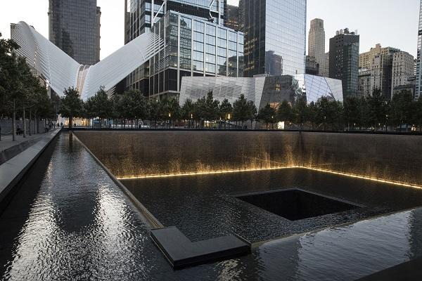 A cloudy sky reflects off the water in the north pool at Memorial plaza. The buildings of lower Manhattan tower over the plaza in the background.