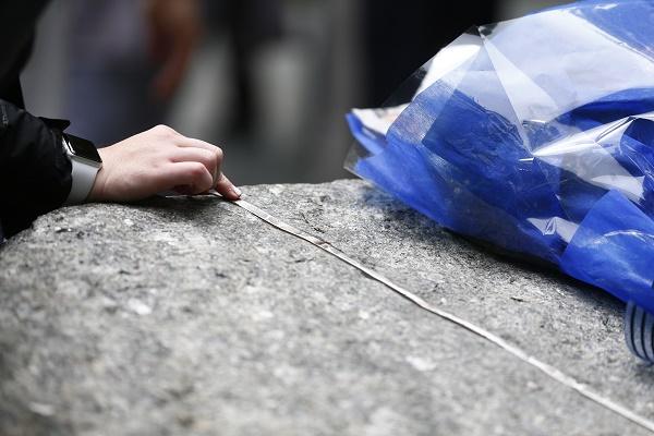 A person places their hand on a granite monolith at the 9/11 Memorial Glade. A bouquet wrapped in a blue flower sleeve sits to the right.