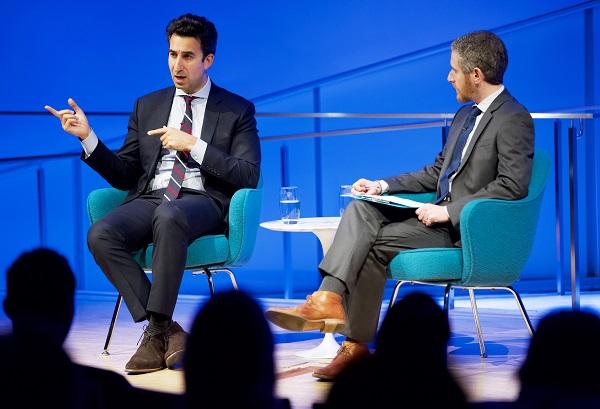 Karim Sadjadpour, an Iran expert, gestures as he speaks onstage at the Museum auditorium. Noah Rauch, senior vice president for education and public programs, sits beside him, holding a clipboard.