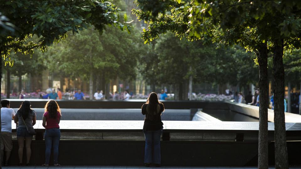 A woman is seen standing at the Memorial parapets at dusk.  She is standing alone with her back to the camera as she takes a photo.  