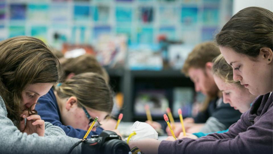 Children at a table look down at their notebooks as they work on a project